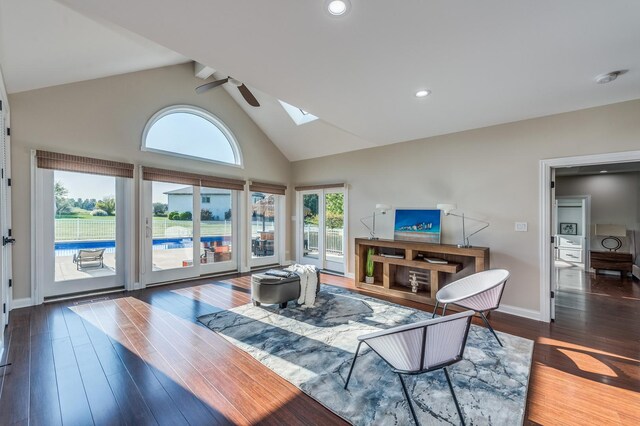 living room with ceiling fan, dark wood-type flooring, high vaulted ceiling, and a skylight