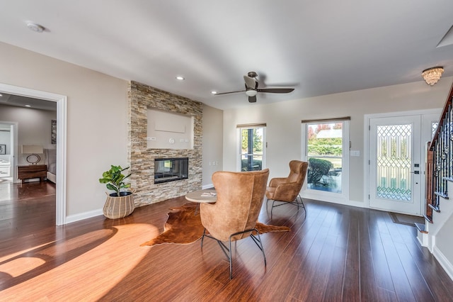 living room with a stone fireplace, ceiling fan, and dark wood-type flooring