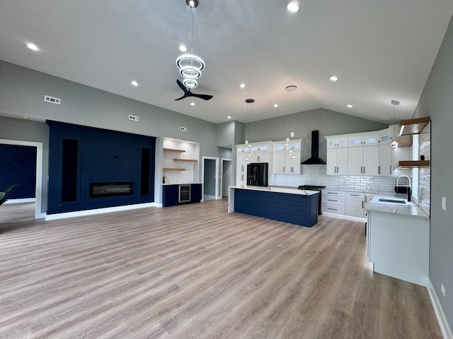 kitchen featuring pendant lighting, a center island, wall chimney exhaust hood, black fridge with ice dispenser, and white cabinetry