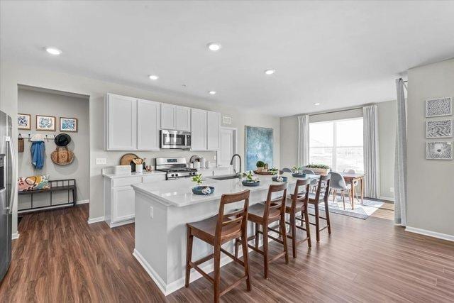 kitchen featuring dark wood-type flooring, a breakfast bar area, a kitchen island with sink, white cabinets, and appliances with stainless steel finishes