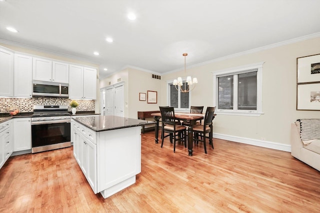 kitchen featuring white cabinets, decorative light fixtures, ornamental molding, and stainless steel appliances