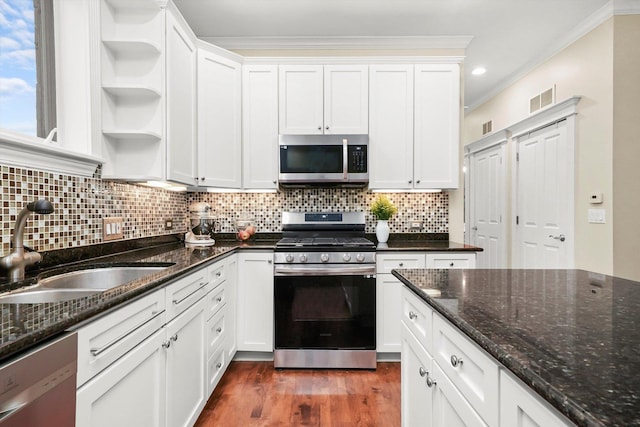 kitchen with sink, dark stone countertops, ornamental molding, appliances with stainless steel finishes, and white cabinetry