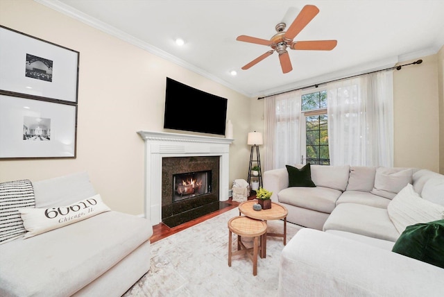 living room with a high end fireplace, hardwood / wood-style flooring, ceiling fan, and crown molding