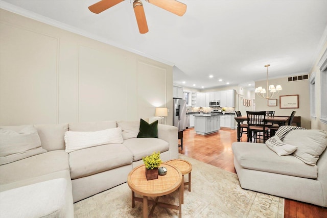 living room featuring ceiling fan with notable chandelier, light hardwood / wood-style flooring, and ornamental molding