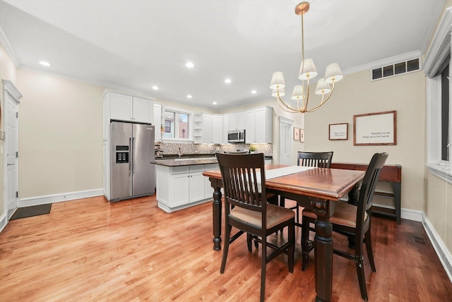 dining area with ornamental molding, light wood-type flooring, and an inviting chandelier