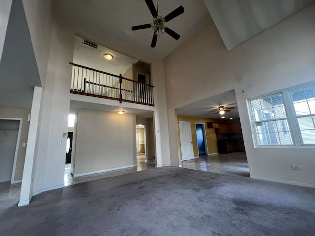 unfurnished living room featuring carpet, ceiling fan, and a towering ceiling