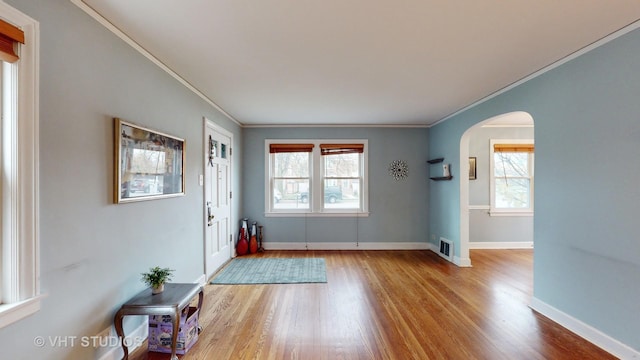 doorway with light hardwood / wood-style floors, crown molding, and a healthy amount of sunlight