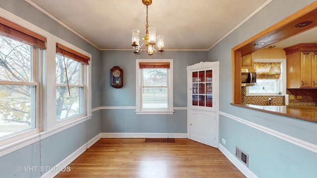 unfurnished dining area with crown molding, sink, a chandelier, and light wood-type flooring