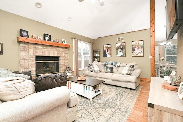 living room with a brick fireplace, ceiling fan with notable chandelier, light hardwood / wood-style flooring, and lofted ceiling