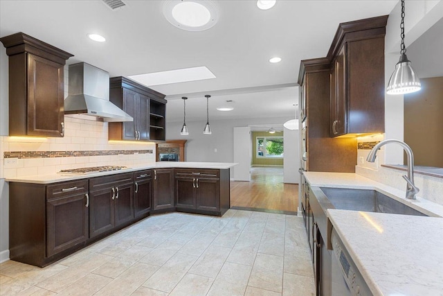 kitchen with stainless steel gas stovetop, backsplash, wall chimney exhaust hood, decorative light fixtures, and kitchen peninsula