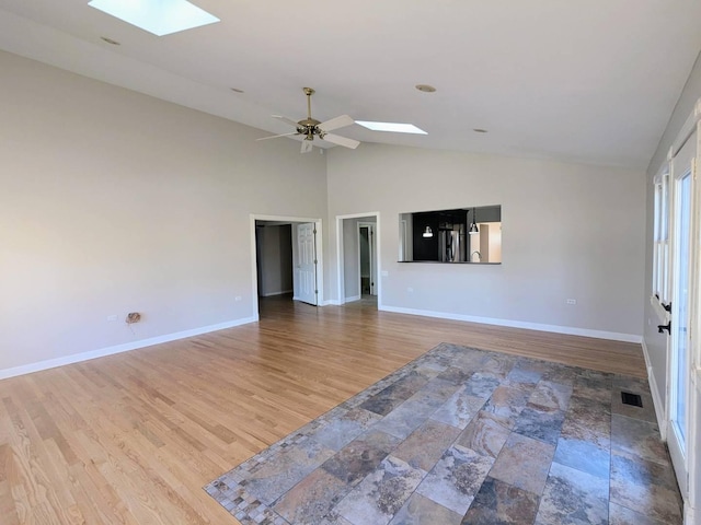 empty room with hardwood / wood-style flooring, ceiling fan, and vaulted ceiling with skylight