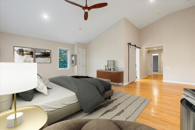 bedroom featuring a barn door, ceiling fan, high vaulted ceiling, and light wood-type flooring