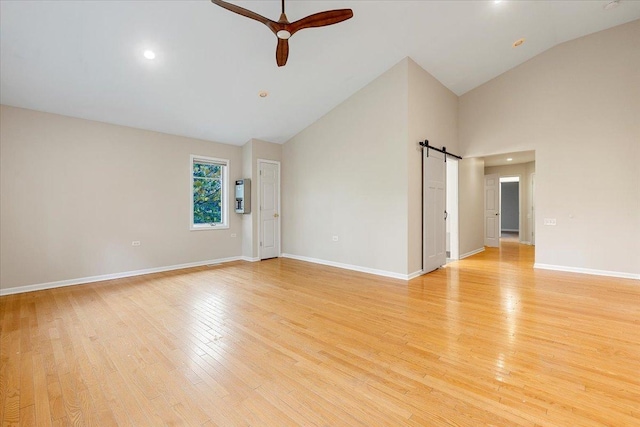 unfurnished room with light wood-type flooring, a barn door, high vaulted ceiling, and ceiling fan