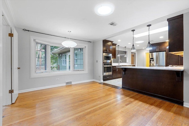 kitchen featuring hanging light fixtures, stainless steel appliances, a breakfast bar area, dark brown cabinets, and ornamental molding