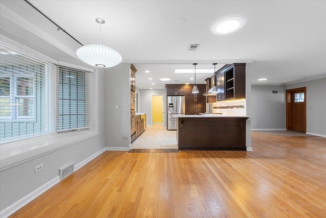 kitchen with stainless steel fridge, tasteful backsplash, dark brown cabinets, wall chimney range hood, and decorative light fixtures