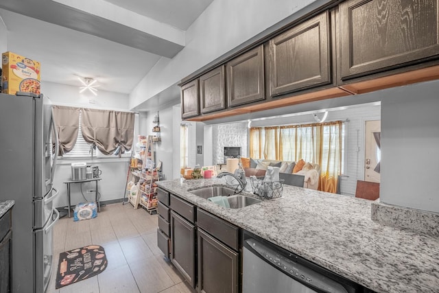 kitchen with light stone countertops, sink, stainless steel appliances, lofted ceiling, and dark brown cabinets