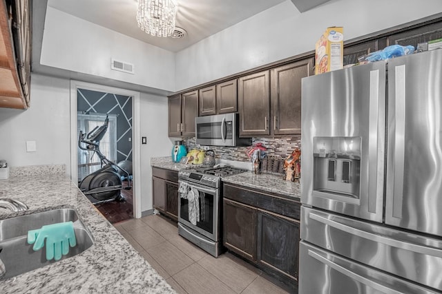 kitchen with sink, light stone countertops, appliances with stainless steel finishes, dark brown cabinets, and a chandelier