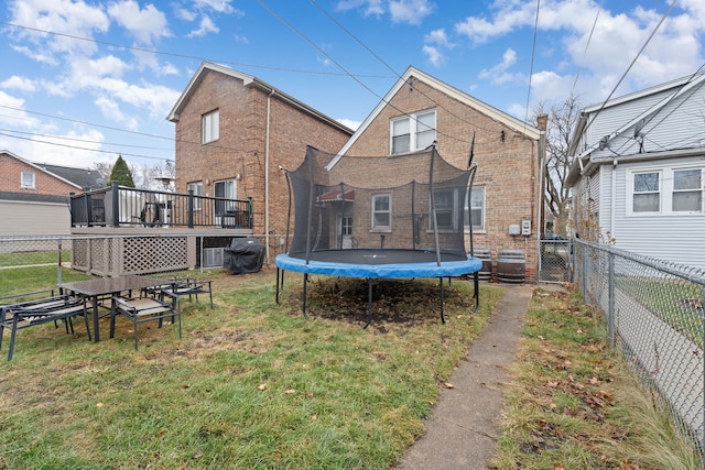 rear view of house with a trampoline, a deck, and a lawn