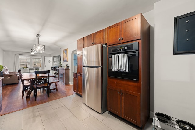 kitchen with black oven, stainless steel refrigerator, hanging light fixtures, and light tile patterned flooring