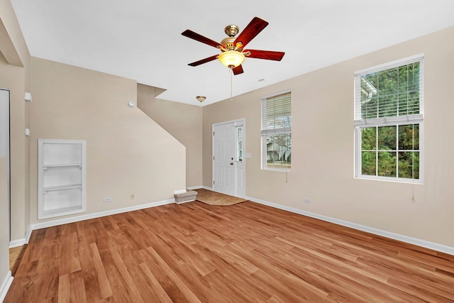 unfurnished living room with built in shelves, ceiling fan, and light wood-type flooring