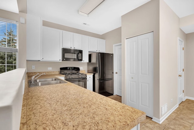 kitchen with sink, stainless steel fridge, range with gas stovetop, white cabinetry, and kitchen peninsula