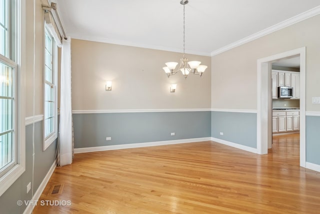 unfurnished room with light hardwood / wood-style flooring, an inviting chandelier, a wealth of natural light, and ornamental molding