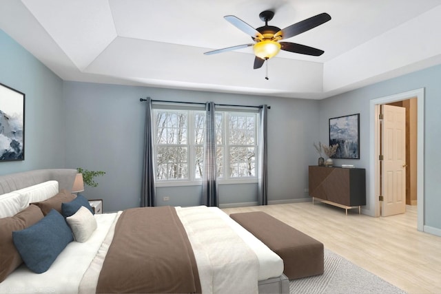 bedroom featuring a raised ceiling, ceiling fan, and light wood-type flooring