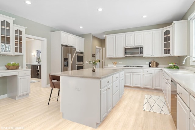 kitchen with sink, a kitchen island, appliances with stainless steel finishes, light hardwood / wood-style floors, and white cabinetry