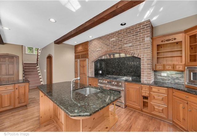 kitchen featuring a kitchen island with sink, high end stainless steel range oven, sink, dark stone countertops, and beam ceiling