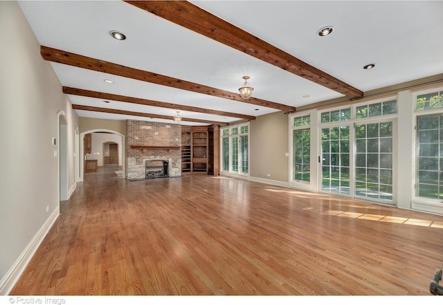 unfurnished living room with a fireplace, light hardwood / wood-style floors, and beamed ceiling