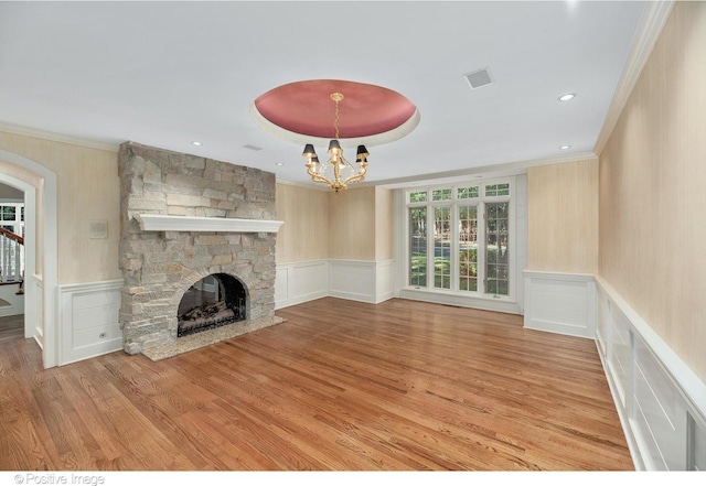 unfurnished living room featuring light hardwood / wood-style floors, a stone fireplace, a notable chandelier, and crown molding