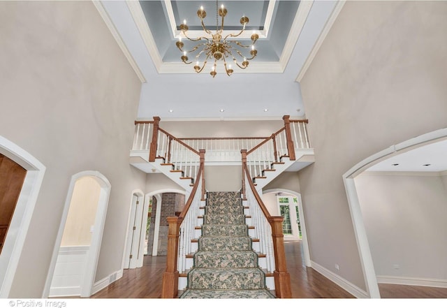 stairs featuring a chandelier, a towering ceiling, hardwood / wood-style flooring, and ornamental molding