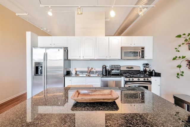 kitchen featuring track lighting, stainless steel appliances, sink, dark stone countertops, and white cabinetry