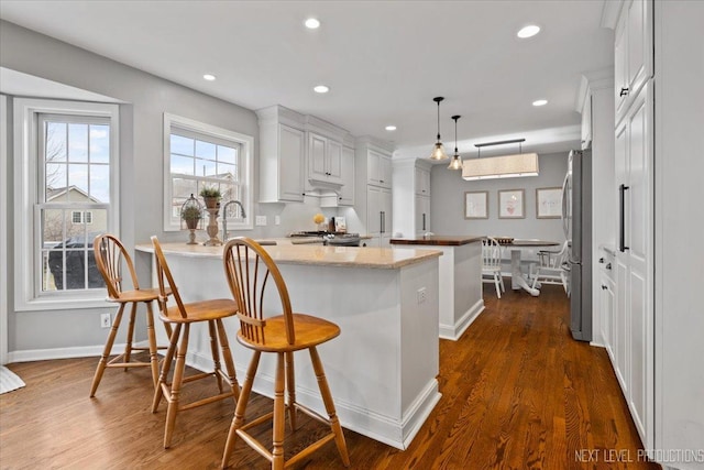 kitchen with a kitchen bar, dark hardwood / wood-style flooring, light stone counters, white cabinetry, and hanging light fixtures