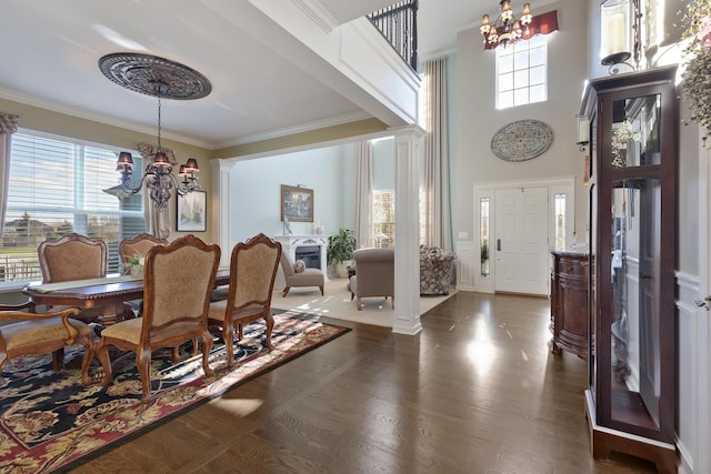 dining space featuring a towering ceiling, ornate columns, ornamental molding, dark wood-type flooring, and an inviting chandelier