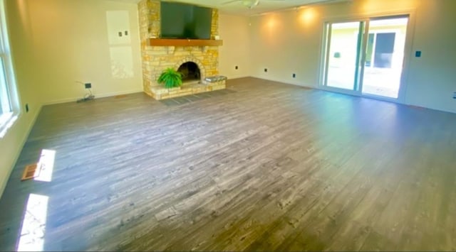 unfurnished living room featuring hardwood / wood-style floors, ceiling fan, and a stone fireplace