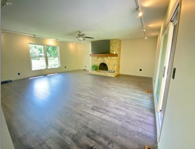 unfurnished living room with rail lighting, ceiling fan, wood-type flooring, and a fireplace