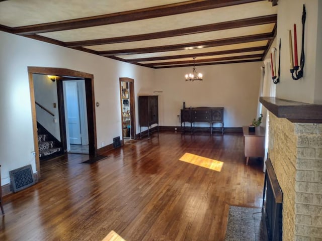 unfurnished living room featuring beam ceiling, dark hardwood / wood-style flooring, a fireplace, and a notable chandelier