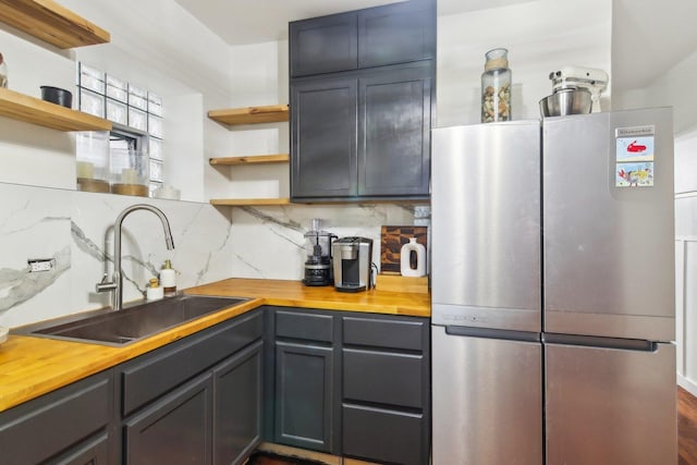 kitchen featuring wooden counters, decorative backsplash, stainless steel refrigerator, and sink