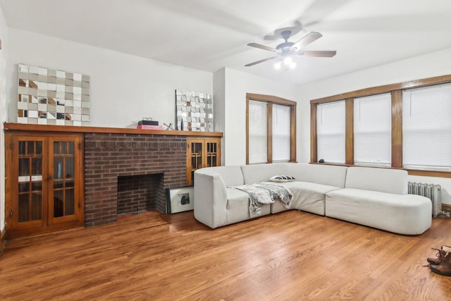 living room featuring radiator heating unit, hardwood / wood-style flooring, a brick fireplace, and ceiling fan