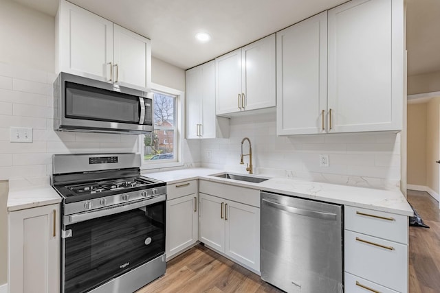 kitchen featuring appliances with stainless steel finishes, light wood-type flooring, light stone counters, sink, and white cabinetry