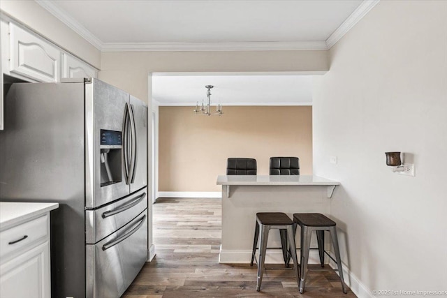 kitchen with stainless steel refrigerator with ice dispenser, crown molding, hardwood / wood-style flooring, white cabinets, and a breakfast bar area