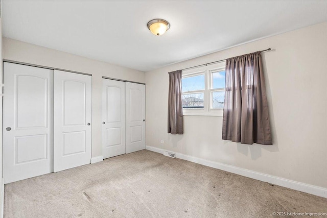 unfurnished bedroom featuring light carpet and two closets