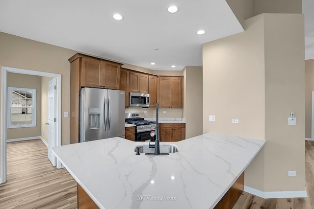 kitchen with light stone countertops, kitchen peninsula, light wood-type flooring, stainless steel appliances, and sink