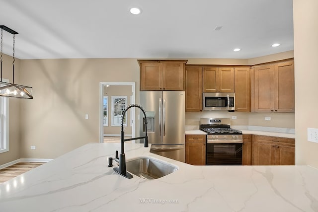 kitchen featuring appliances with stainless steel finishes, light stone counters, sink, wood-type flooring, and hanging light fixtures