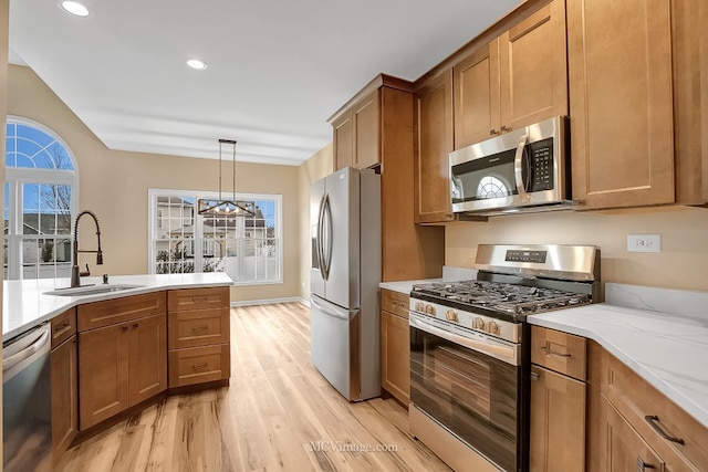 kitchen with light stone countertops, appliances with stainless steel finishes, sink, decorative light fixtures, and light hardwood / wood-style floors