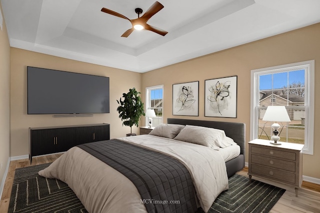 bedroom with a raised ceiling, multiple windows, ceiling fan, and light hardwood / wood-style floors