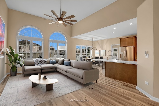 living room with sink, ceiling fan with notable chandelier, and light hardwood / wood-style flooring