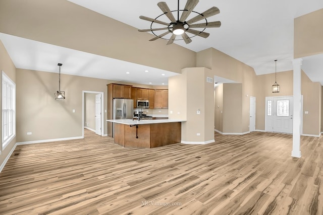 kitchen with hanging light fixtures, a high ceiling, kitchen peninsula, light hardwood / wood-style floors, and appliances with stainless steel finishes