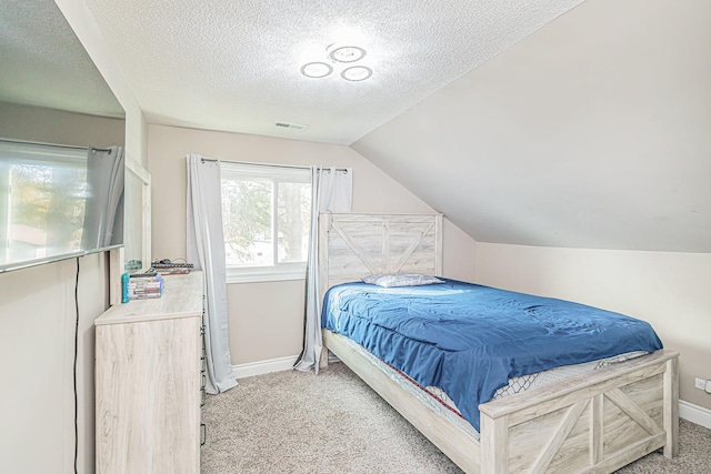 bedroom with vaulted ceiling, light carpet, and a textured ceiling